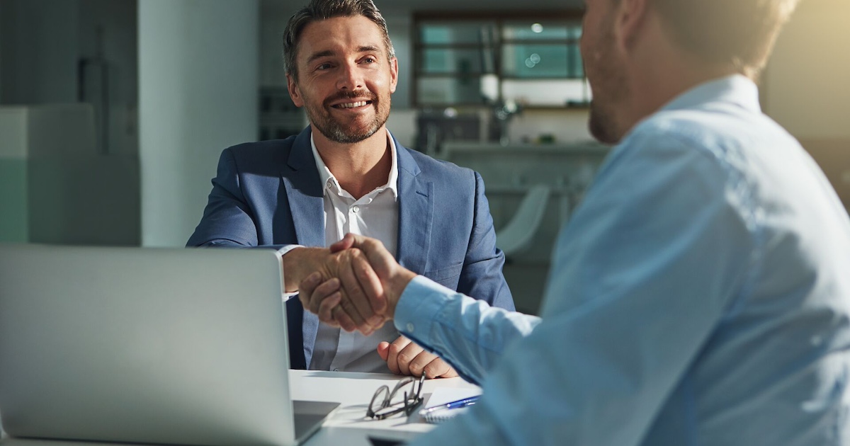 Two people shaking hands from opposite sides of the table