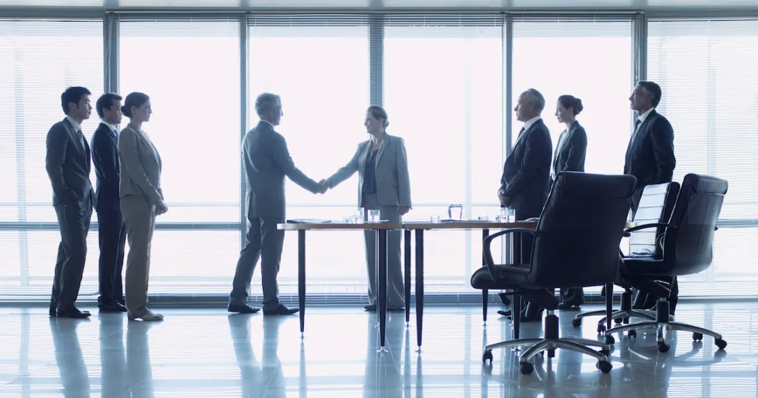 Two people shaking hands in front of a large window while six other people watch