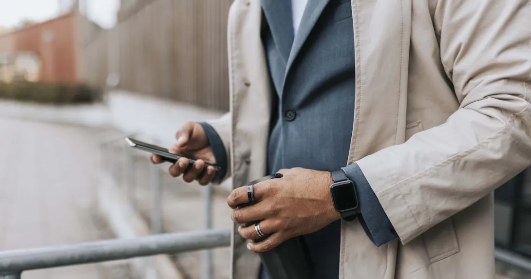 Midsection of a person in a suite wearing two rings and looking at their phone