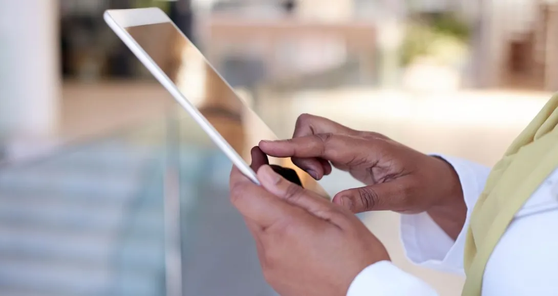 Person wearing a white long sleeve shirt with a yellow scarf holding a tablet