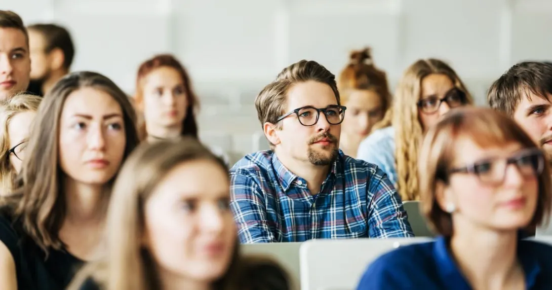 
  Numerous students sitting in a classroom with a vantage point from the front
